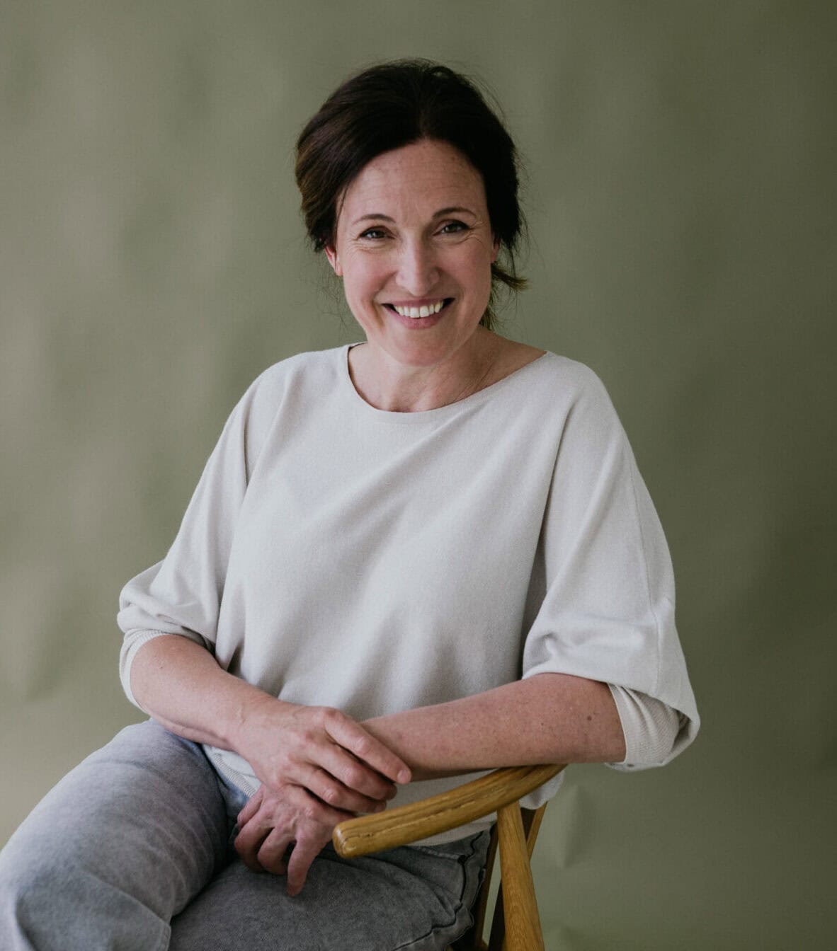 Glimlachende Margo Vermeiren, zittend op een stoel voor een groene achtergrond