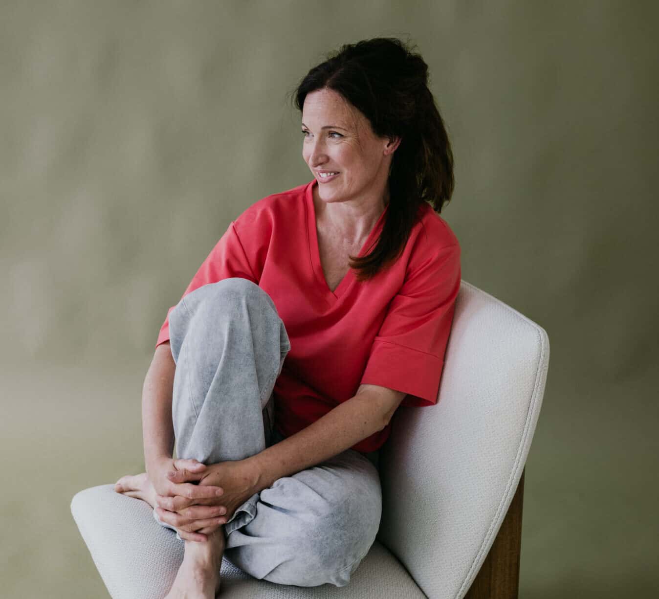 Glimlachende Margo Vermeiren in rood t-shirt, zittend op een witte stoel